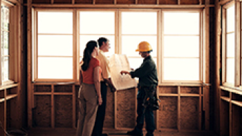 Drei Personen stehen in einem Rohbau und schauen auf einen Plan 