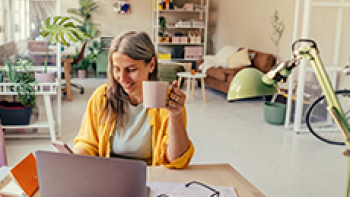 Frau mit Kaffeetasse in der Hand arbeitet am Laptop
