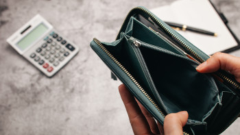 Eine leere Geldbörse, im Hintergrund ein Schreibblock und ein Taschenrechner