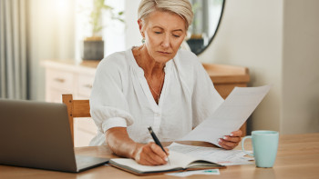 Ältere Frau mit Notebook, die zuhause Papierkram erledigt