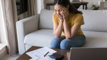 Frau sitzt mit verzweifelter Mimik am Couchtisch vor Formularen und Laptop 
