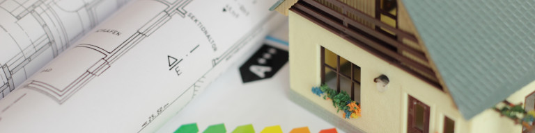 Energetische Sanierung Bauplan und Energieeffizienzskala auf dem ein Modellhaus steht