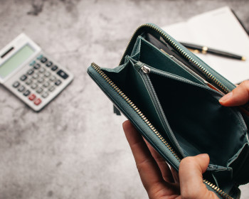 Eine leere Geldbörse, im Hintergrund ein Schreibblock und ein Taschenrechner