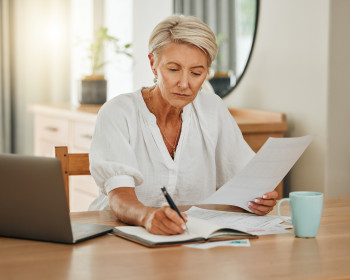 Ältere Frau mit Notebook, die zuhause Papierkram erledigt