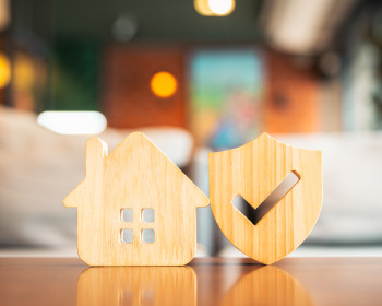 Holzhäuschen und Versicherungssymbol auf einem Tisch 