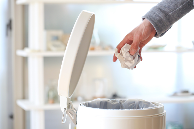 Hand wirft Papier in den Mülleimer