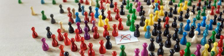 Viele farbige Spielfiguren scharen sich um ein Wahlkreuz in der Mitte