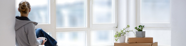Frau schaut neben Umzugskartons aus dem Fenster