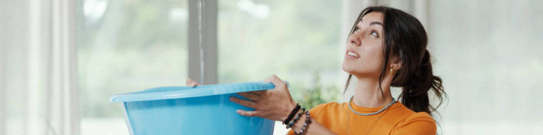 Frau fängt von der Decke tropfendes Wasser auf