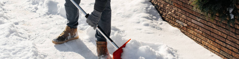 Mann mit Schneeschaufel räumt Weg
