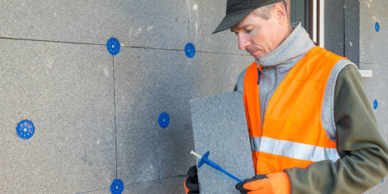 Handwerker befestigt Außendämmung an Fassade