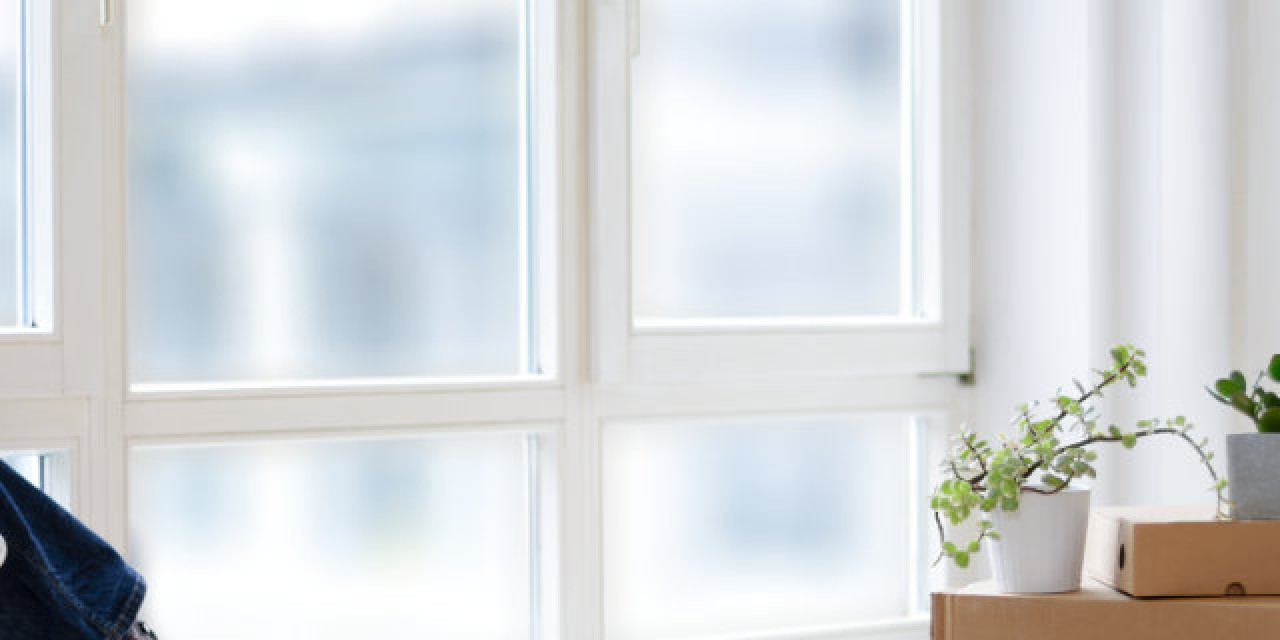 Frau sitzt neben Umzugskartons am Fenster einer Stadtwohnung