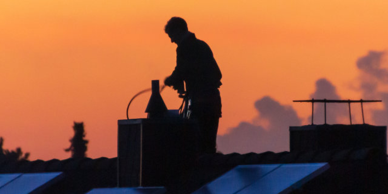 Schornsteinfeger beim Reinigen auf dem Hausdach