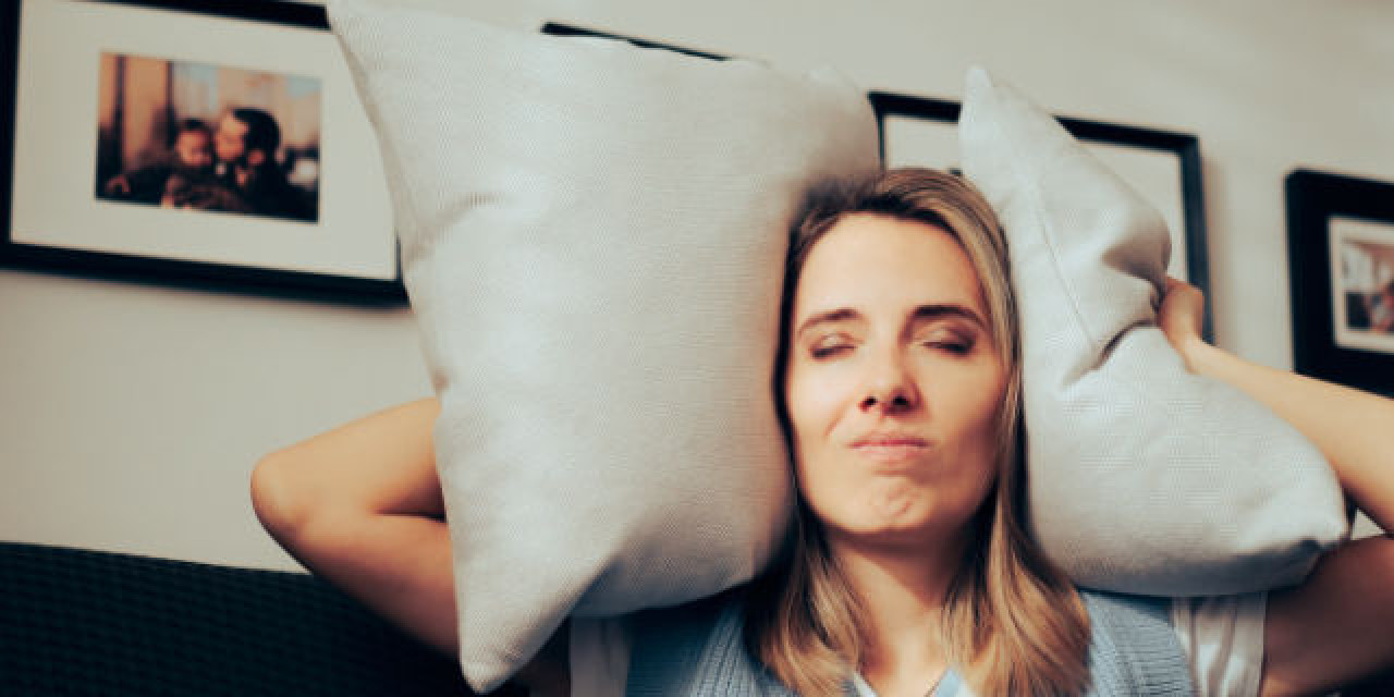 Frau leidet unter Lärm und hält sich Kissen vor die Ohren