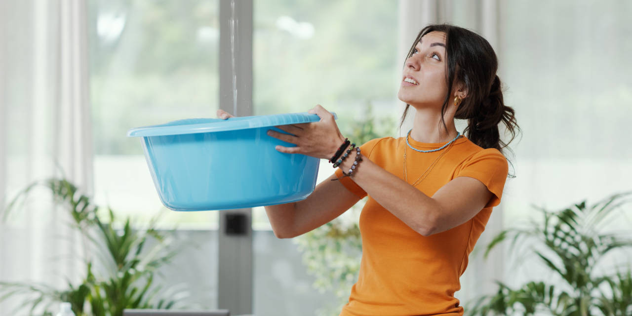 Frau fängt von der Decke tropfendes Wasser auf