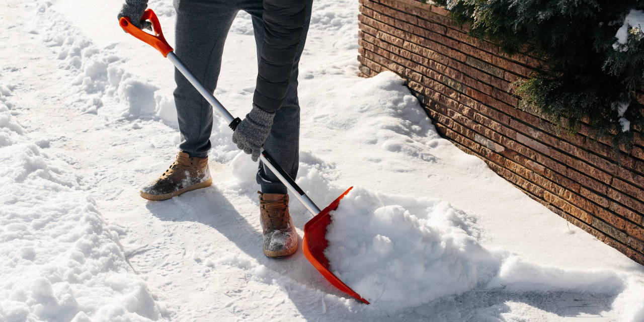 Mann mit Schneeschaufel räumt Weg