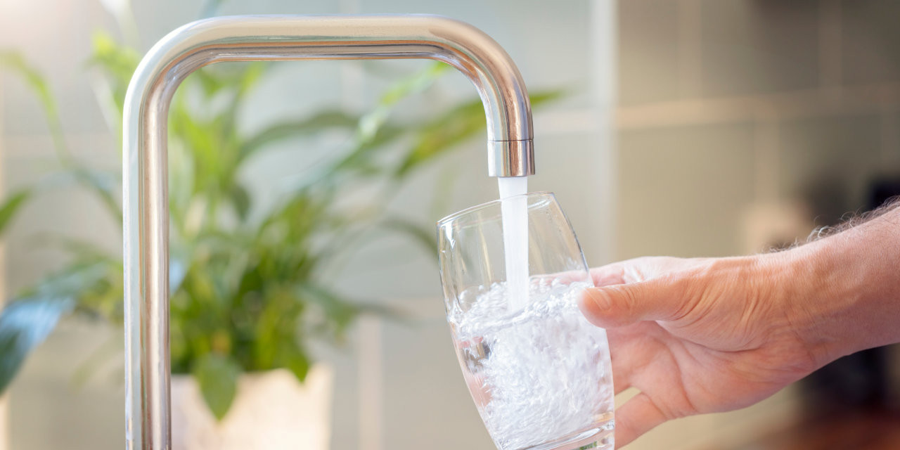 Glas wird an Wasserhahn mit Trinkwasser gefüllt