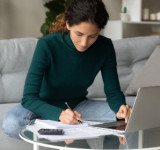 Frau mit Papieren und Laptop auf dem Sofa