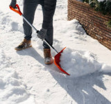 Mann mit Schneeschaufel räumt Weg