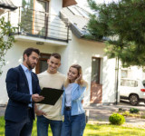 Immobilienmakler  und junges Paar vor Einfamilienhaus, Hauskauf