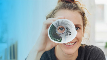 Frau guckt mit einem Auge durch Zeitungsrolle