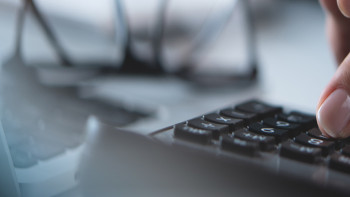 Hand hält Bleistift über Taschenrechner mit sichtbaren Tasten und Display.