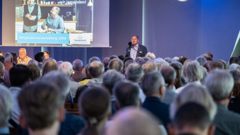 Mann spricht vor großem Publikum in einem Saal mit Präsentationsfolie im Hintergrund