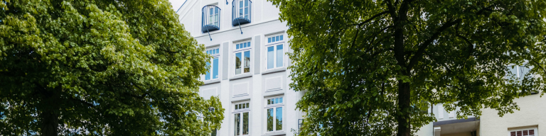 Fassade eines Hauses mit grünen Bäumen links und rechts