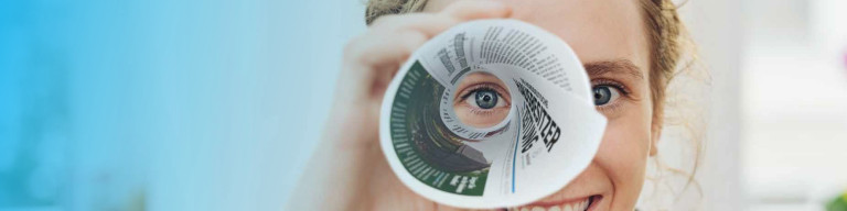 Frau guckt mit einem Auge durch Zeitungsrolle