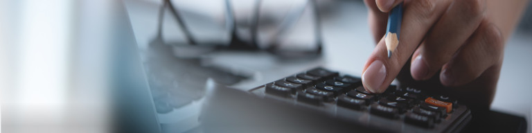 Hand hält Bleistift über Taschenrechner mit sichtbaren Tasten und Display.