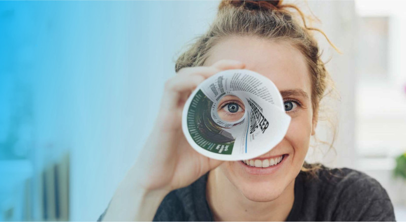 Frau guckt mit einem Auge durch Zeitungsrolle