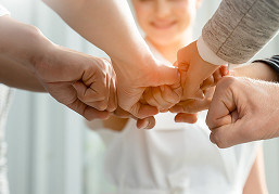 Mehrere Hände unterschiedlicher Personen formen einen gemeinsamen Fauststoß in der Bildmitte.