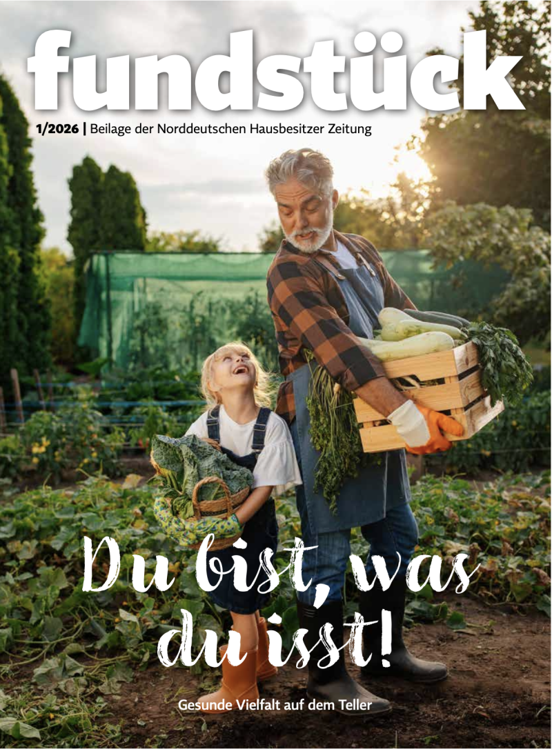 Zwei Personen stehen in einem Garten, eine trägt eine Holzkiste mit Gemüse, die andere hält einen Korb mit Kohl.