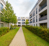 Moderner Wohnkomplex mit mehrstöckigen Gebäuden, zentralem Gehweg, Rasenflächen, Hecken und Bäumen