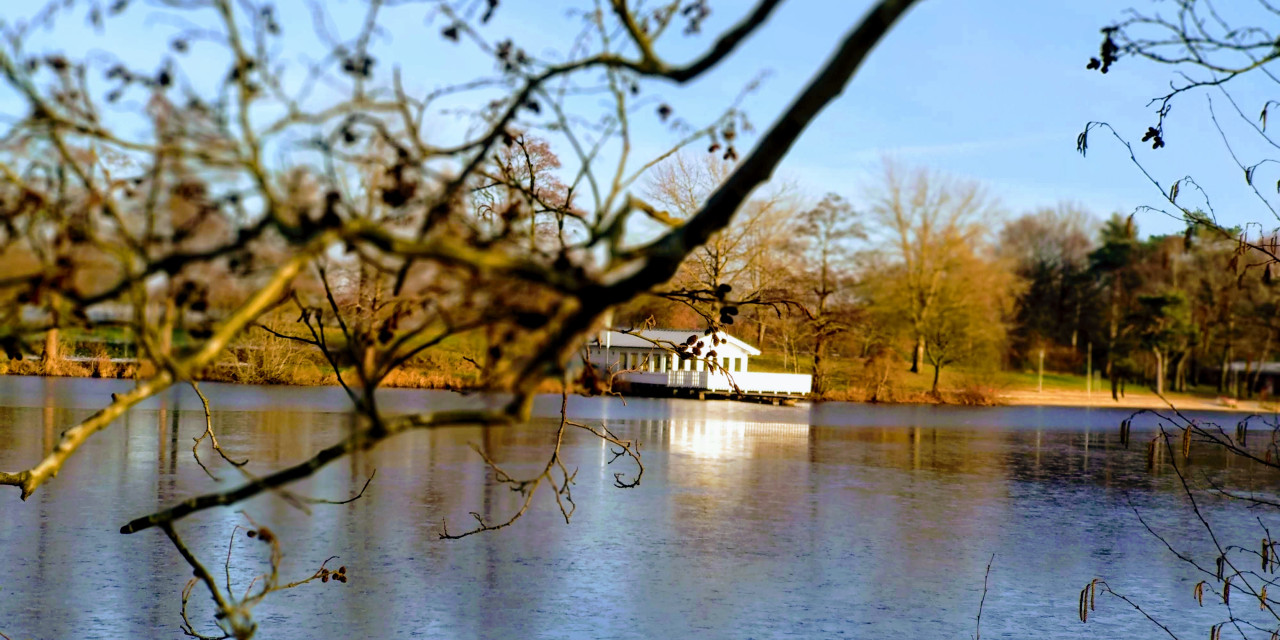 Bild von einem See mit einem Haus und blauem Himmel